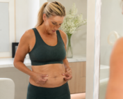 Woman examining loose abdominal skin after weight loss in a bright modern setting